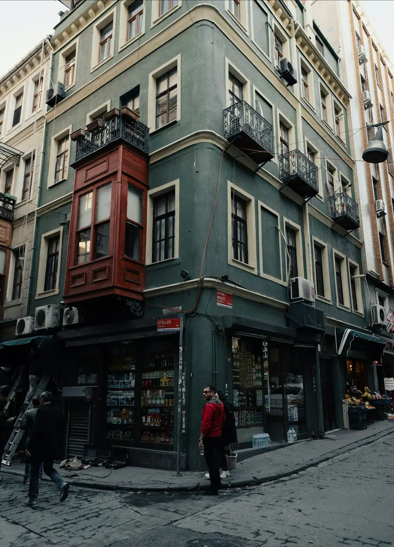 İstanbul'da bir sokak köşesi: yeşil ve kırmızı cumbalı apartman, önünden geçen insanlar