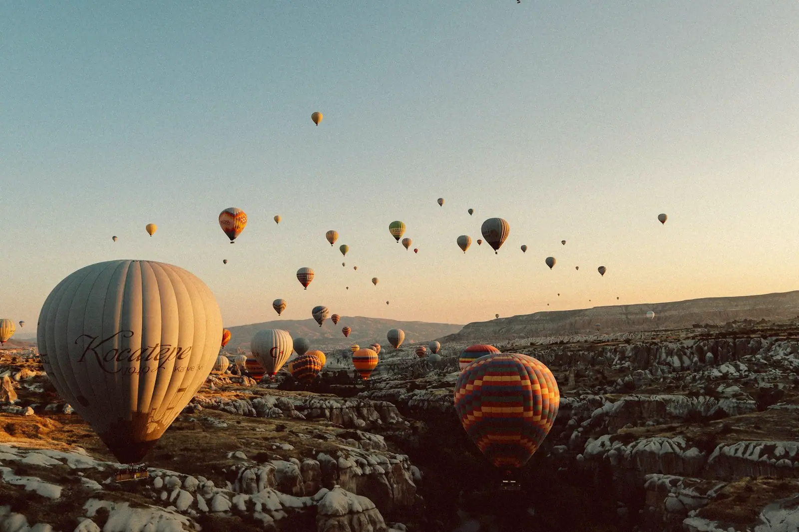 Kapadokya'da gün doğarken vadinin üzerinde yükselen onlarca sıcak hava balonu